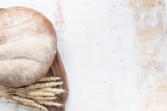 Fresh bread and wheat stems on the cutting board on the rustic white table flat lay background with copy space.