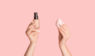 Close up of female hands showing bottle of cosmetic foundation and sponge on pink background, panorama - Powered by Adobe