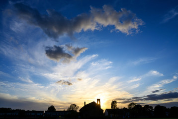 Fototapeta premium Dramatic clouds at sunset over St Johns Church in Beckenham, Kent, UK. The setting sun shines through the bell tower of the church. Beautiful clouds and evening sky at sunset with church silhouette.