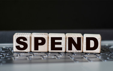 concept word SPEND on cubes on the background of a laptop
