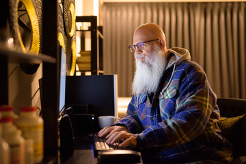 Obraz na płótnie Canvas Mature bald bearded hipster man working overtime at home late at night