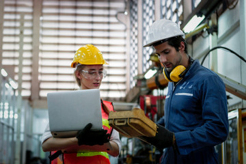 Industrial engineer worker woman and man wearing helmet discussing and working together with robot arm for arduino mechanism at manufacturing plant factory, young people working in industry