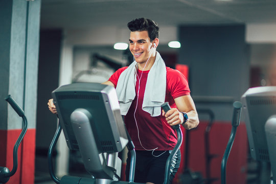 Young man doing exercise on elliptical cross trainer in sport fitness gym club
