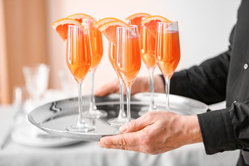 Waiter with glasses of tasty mimosa cocktail at banquet