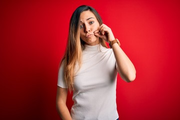 Beautiful blonde woman with blue eyes wearing casual white t-shirt over red background mouth and...