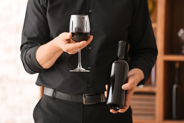 Man with bottle and glass of tasty wine in cellar