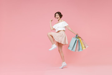 Happy young woman girl in summer clothes hold package bag with purchases isolated on pastel pink background studio portrait. Shopping discount sale concept. Mock up copy space. Doing winner gesture.