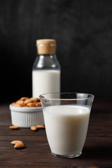 Almond milk in a glass and a glass bottle on dark wooden background.