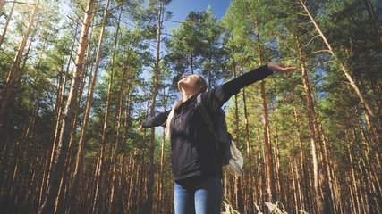 Toned photo of beautiful smiling female stretching hands and enjoying warm sun light in pine tree forest. Concept of freedom and harmony with nature.