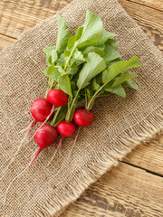 Ripe red radishes with green leaves on sackcloth and wooden boards.
