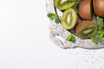 top view of juicy kiwi fruits near green peppermint on silver plate on white