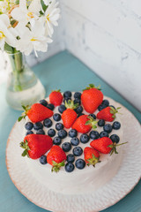 Beautiful summer cake with strawberry, blueberry and narcissus flowers on blue table