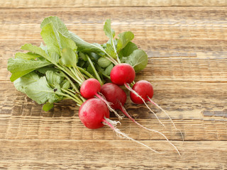 Ripe red radishes with green leaves on wooden boards.