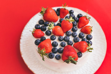 A tasty summer pie or cake with strawberries and blueberries on white plate on red background. Delicious dessert