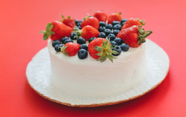 Side view of tasty summer cream cake with strawberries and blueberries on white plate on red background. Delicious dessert with berries