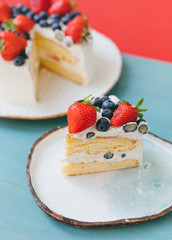 A piece of sweet delicious sponge cake with whipped cream and summer fresh berries on hand made plates on light blue wooden table. No diet. Selective focus