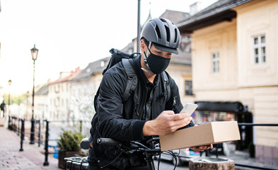 Delivery man courier with face mask and smartphone delivering parcel box in town.