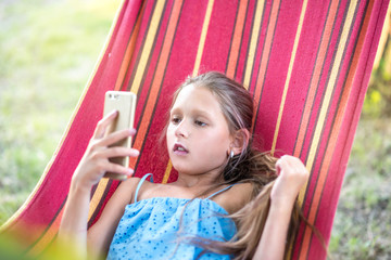 A pretty girl is resting on a hammock. Girl makes selfie on the phone. Family content. Rest on a summer day. smiling child.