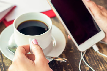 Smartphone with black screen in woman hands with cup of coffee on the table in cafe.