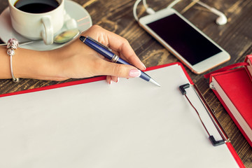Left hand of business woman begining to write in the empty sheet of paper on the table at the cafe.