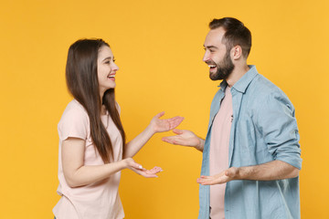 Side view of cheerful young couple two friends guy girl in casual clothes posing isolated on yellow background. People lifestyle concept. Mock up copy space. Looking at each other, speaking talking.