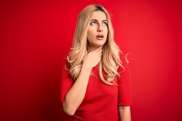 Young beautiful blonde woman wearing casual t-shirt standing over isolated red background Touching painful neck, sore throat for flu, clod and infection