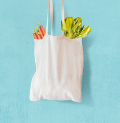 White  textile grocery shopping bag with vegetables hanging at light blue background. Copy space. Zero waste concept. Cotton reusable bag. Plastic free shopping. Eco friendly bag mock up.