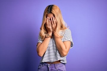 Young beautiful blonde woman wearing striped t-shirt and glasses over purple background rubbing eyes for fatigue and headache, sleepy and tired expression. Vision problem