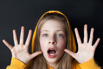 Fototapeta premium Teenager girl in an orange sweatshirt with bright emotions on her face on a black background. Selective focus. Side view