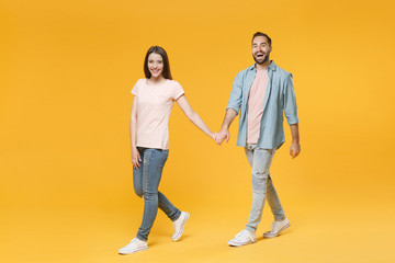 Obraz premium Cheerful young couple two friends guy girl in pastel blue casual clothes posing isolated on yellow background studio portrait. People lifestyle concept. Mock up copy space. Walking, holding hands.