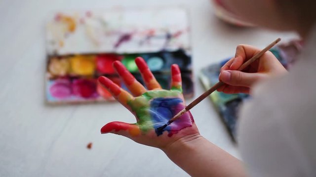 Close-up of a child is hand. A girl sits on the floor and paints a rainbow in the palm of her hand. Quarantine. Stay at home. Flash mob society community on self-isolation 