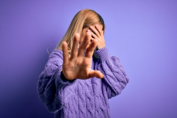 Young beautiful blonde woman wearing casual turtleneck sweater over purple background covering eyes with hands and doing stop gesture with sad and fear expression. Embarrassed and negative concept.