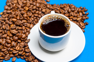 heart shaped coffee beans and cup with coffee on blue background