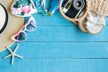 Flat lay of summer accessories with colorful bikini, sunglasses, beach hat, sunscreen, bag, camera and slippers on blue wooden background, copy space, top view. Tropical summer concept.