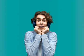 Cant take my eyes off. Portrait of a young beautiful man wearing white t-shirt and blue shirt in headphones propping head with fists. With loving gaze