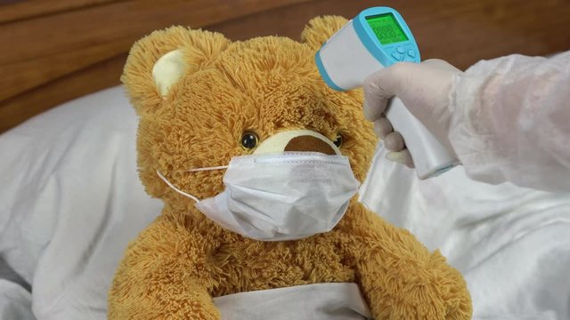 A teddy bear is measured with an infrared thermometer. The doctor makes a temperature measurement with a thermometer pistol. The green light lights up to indicate normal temperature.