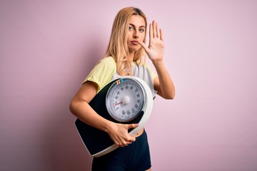 Young beautiful blonde sporty woman on diet holding weight machine over pink background with open...