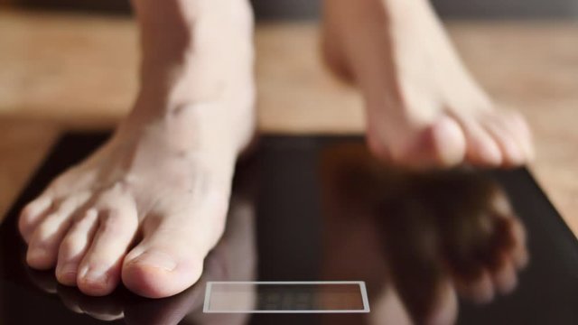 A woman measures her weight on a bathroom scale. Young woman gets up on the scales close-up.
