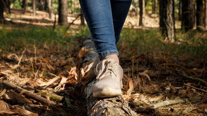 Closeup image of woman wearing sneakers walking and balancing on log on ground at forest