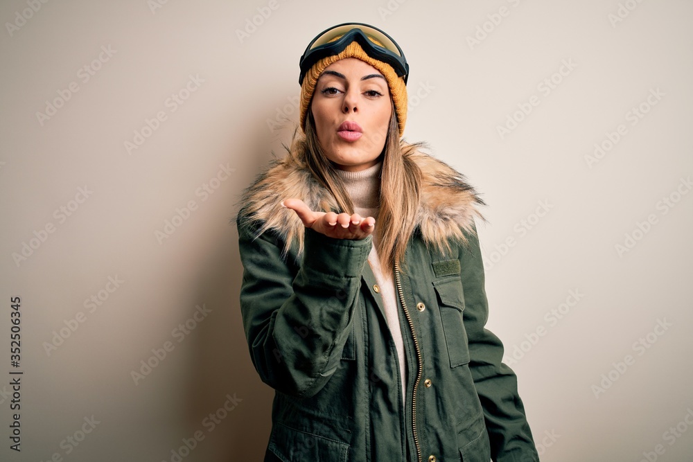 Sticker young brunette skier woman wearing snow clothes and ski goggles over white background looking at the