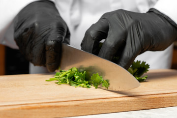 A cook in black gloves is cutting parsley.