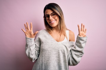 Young beautiful brunette woman wearing casual sweater and glasses over pink background showing and pointing up with fingers number nine while smiling confident and happy.