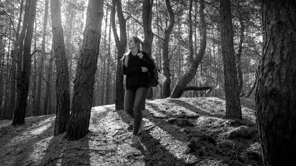 Black and white photo of beautiful young woman with backpack hiking in the old forest