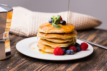 Maple syrup pouring over a stack of mini pancakes.