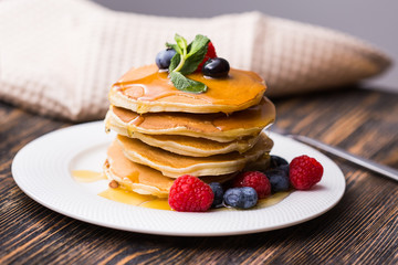 Pancakes with blueberries and raspberry and maple syrup on wooden background. Breakfast and...