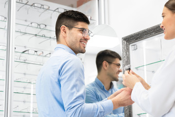 Naklejka na ściany i meble Optometrist helping young guy to choose glasses