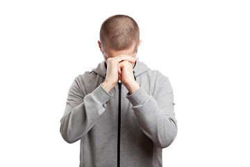 faithful praying male athlete in prayer folded his hands together to each other, his head lowered to the bottom. Dressed in a gray hooded jacket, short haircut. Isolated