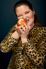 Girl in a beautiful leopard shirt eats an apple. Overweight.