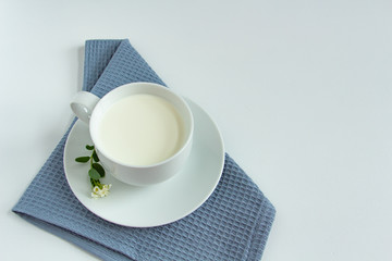 a white cup of fresh milk on a white background with sprigs of white flowers that complement the composition, tasty, healthy, atmospheric
