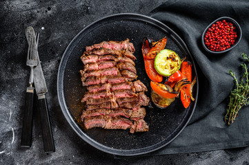 Sliced Grilled beef marbled rare steak. Chuck eye roll on a plate with a side dish of vegetables. Black background. Top view